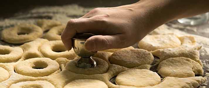 person hand pressing shapes into doughnut dough