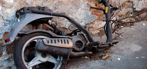 Broken motorbike missing a wheel and dumped by a wall.