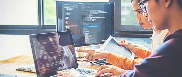 two people working on code on a computer and laptop