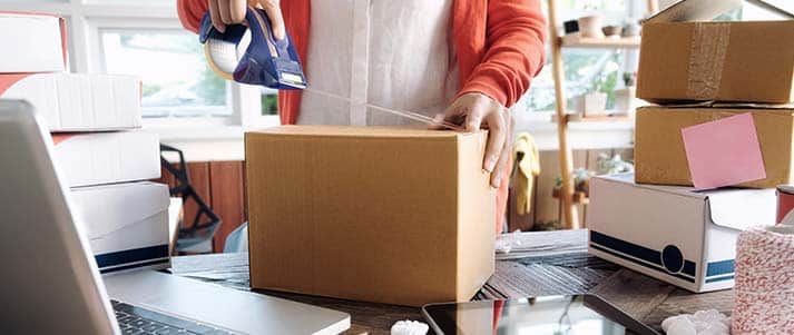 woman putting tape on a parcel on a desk with laptop